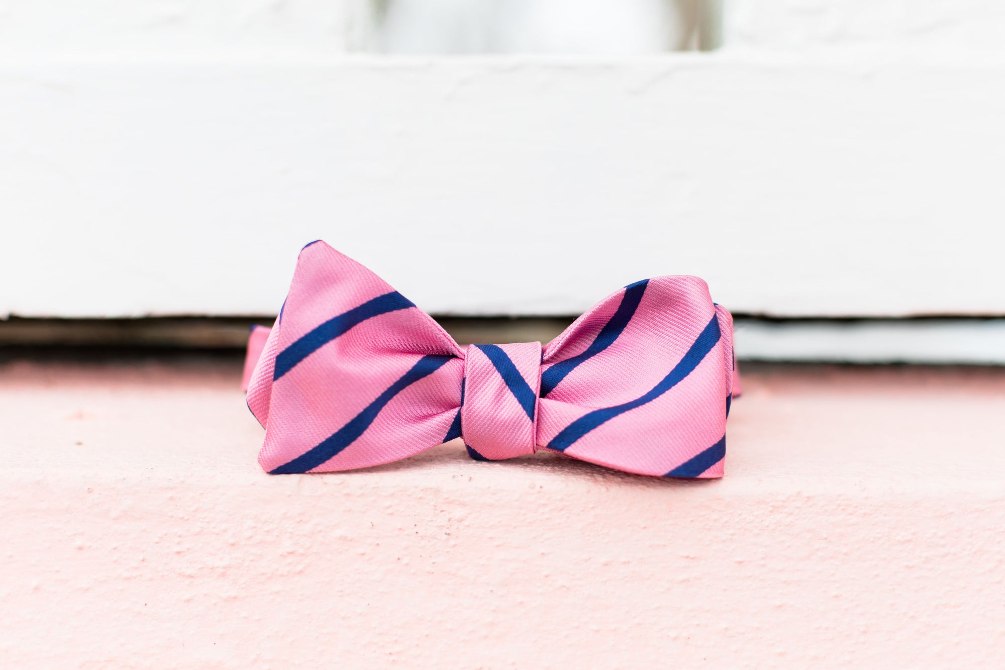 Men's pink bow tie. 100% silk with a blue striped design.